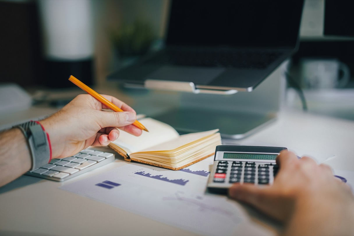 Una calculadora y un cuaderno sobre un escritorio, usados para calcular precios